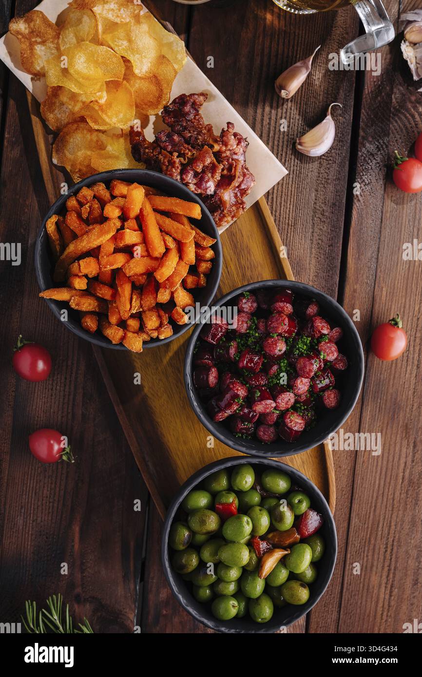 Cibo, vista sopraelevata di spuntini salati, tra cui noci, patatine e olive, presentati su un tavolo rustico Foto Stock