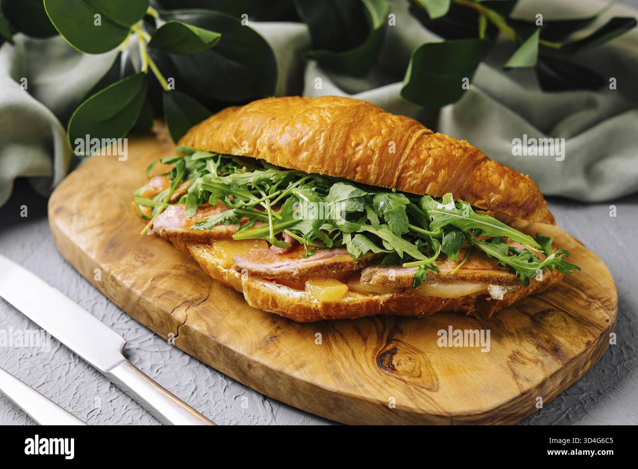 Cibo, delizioso panino con croissant ripieno di pancetta, rucola e formaggio su un tavolo di legno Foto Stock