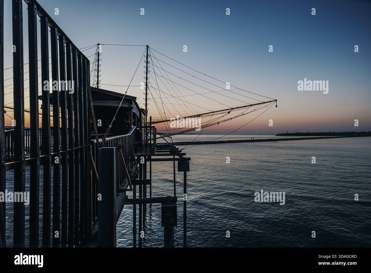 Trabocco, una tradizionale struttura di pesca, che si estende nel calmo mare Adriatico al tramonto, con intricate piattaforme e reti in legno. Foto Stock