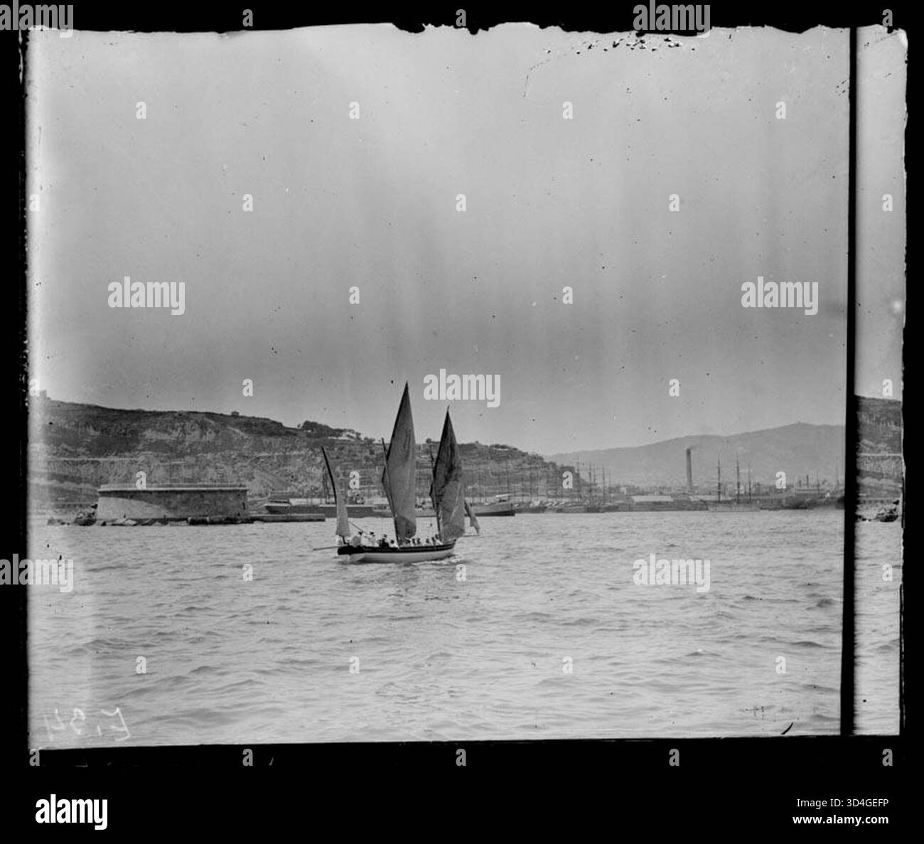 Una nave sul mare con il porto di Barcellona sullo sfondo, catturata da Antoni Bartumeus i Casanovas tra il 1897 e il 1925. L'immagine mostra il trasporto marittimo e la vivace attività del porto. Foto Stock