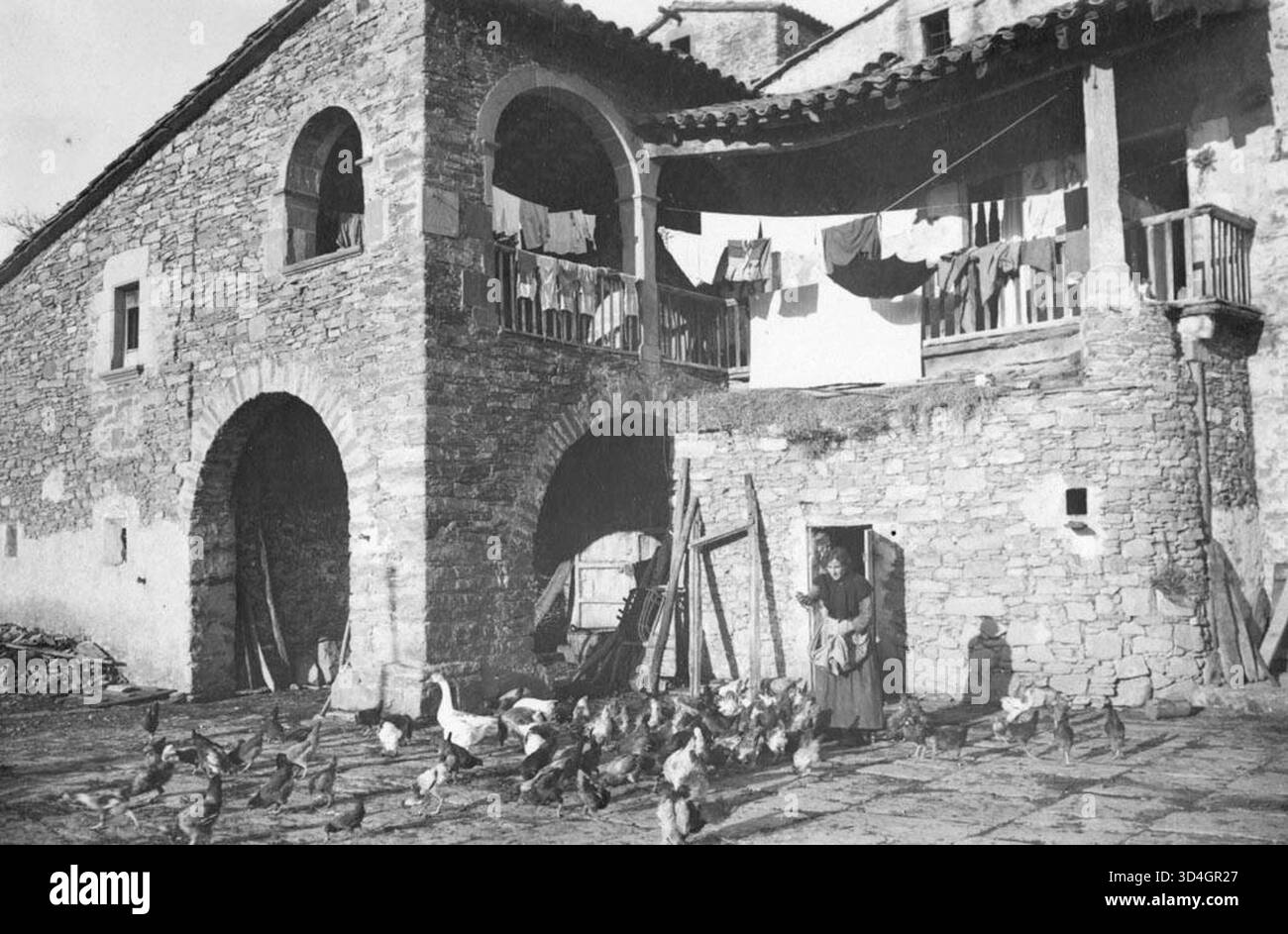Il pavimento della trebbiatura e la facciata del portico di El Joglar con una donna che dà da mangiare al pollame, catturato da Josep Garrut i sala intorno al 1931. L'immagine mostra la vita rurale e la tradizionale architettura catalana in campagna. Foto Stock