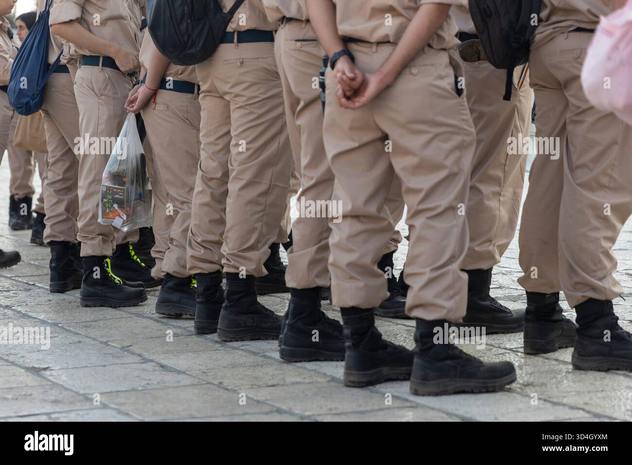 Primo piano di una linea di corpi inferiori dei soldati israeliani, mostrando i pantaloni kaki e gli stivali militari neri, con uno che tiene una piccola borsa di plastica. Foto Stock