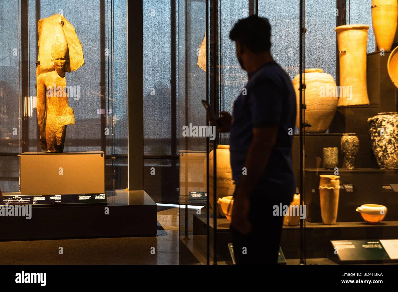 Un passaggio turistico tra antichi manufatti e statue egiziane con le piramidi mostrate sullo sfondo Foto Stock