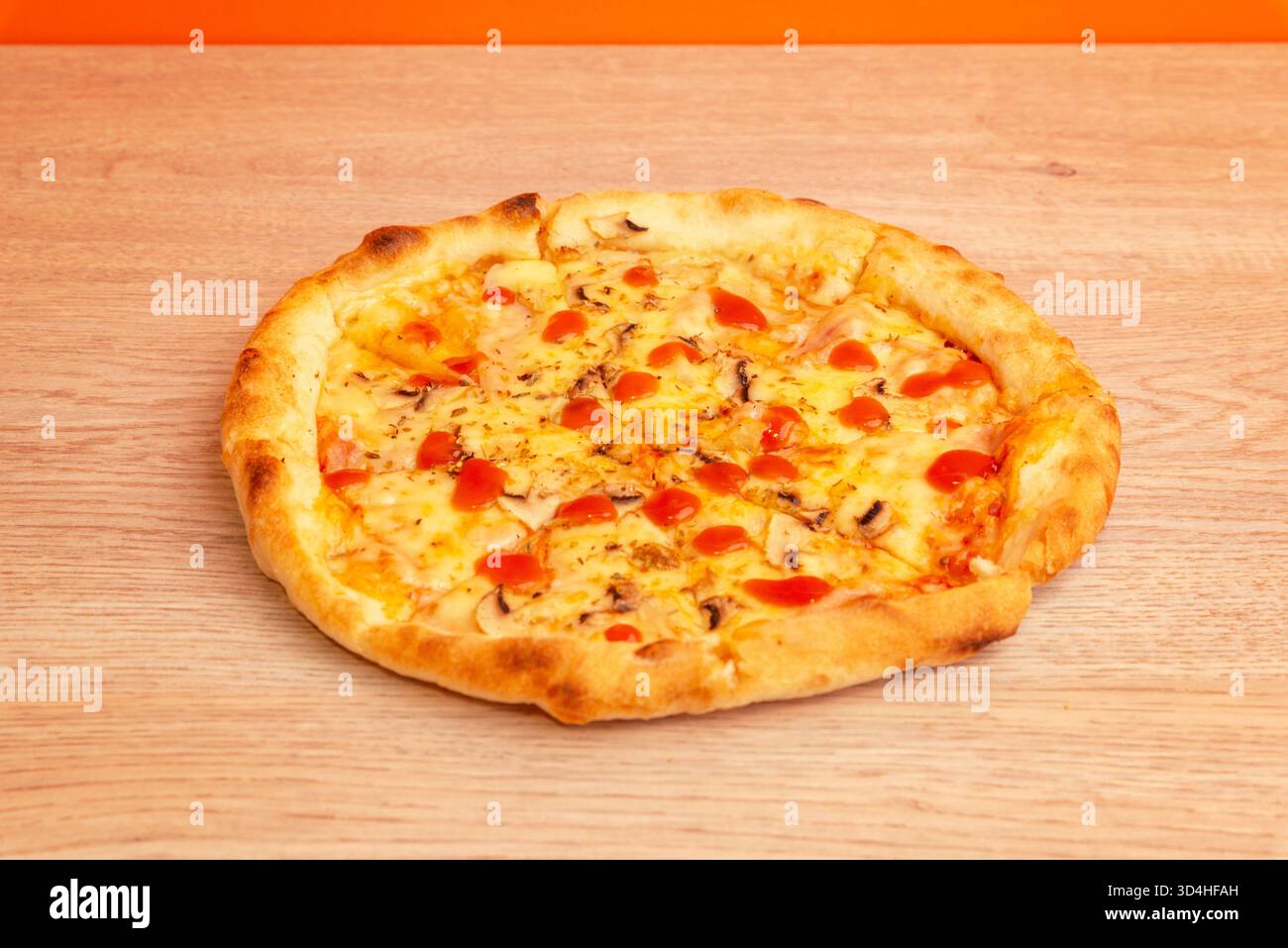 Pizza calda con salsa di pomodoro e formaggio fuso su un tavolo di legno in un accogliente interno della cucina, bottiglie di olio d'oliva sfocate sullo sfondo Foto Stock