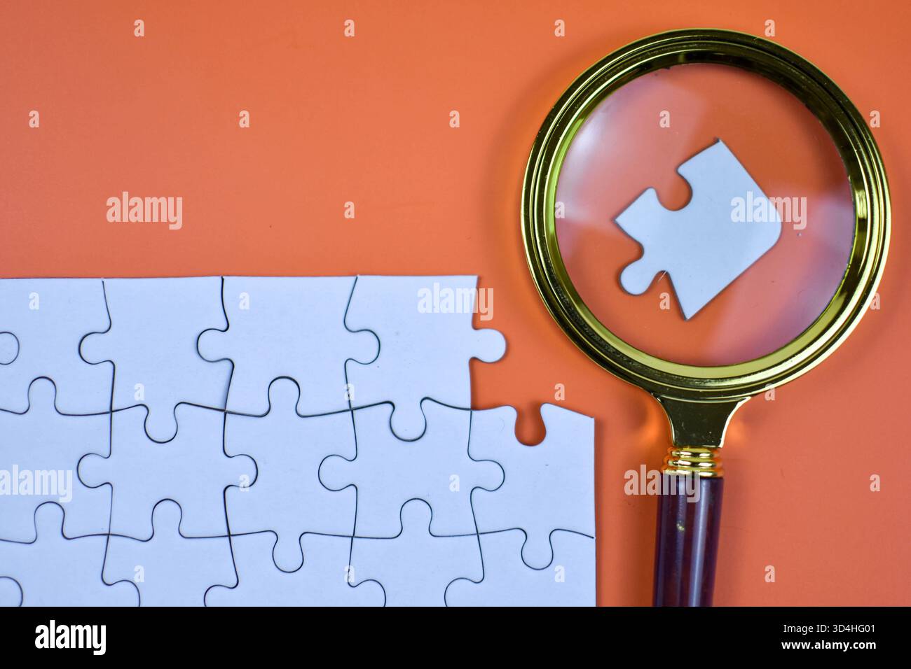 La lente d'ingrandimento sul puzzle bianco evidenzia il pezzo mancante su sfondo arancione, simboleggiando la ricerca mirata e avvicinandosi al completamento dell'attività strutturata Foto Stock