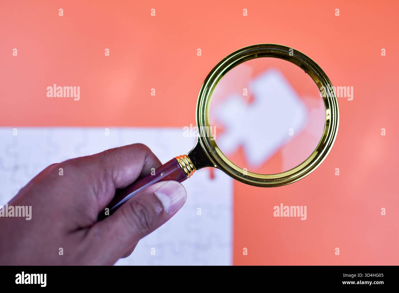 La lente d'ingrandimento sul puzzle bianco evidenzia il pezzo mancante su sfondo arancione, simboleggiando la ricerca mirata e avvicinandosi al completamento dell'attività strutturata Foto Stock