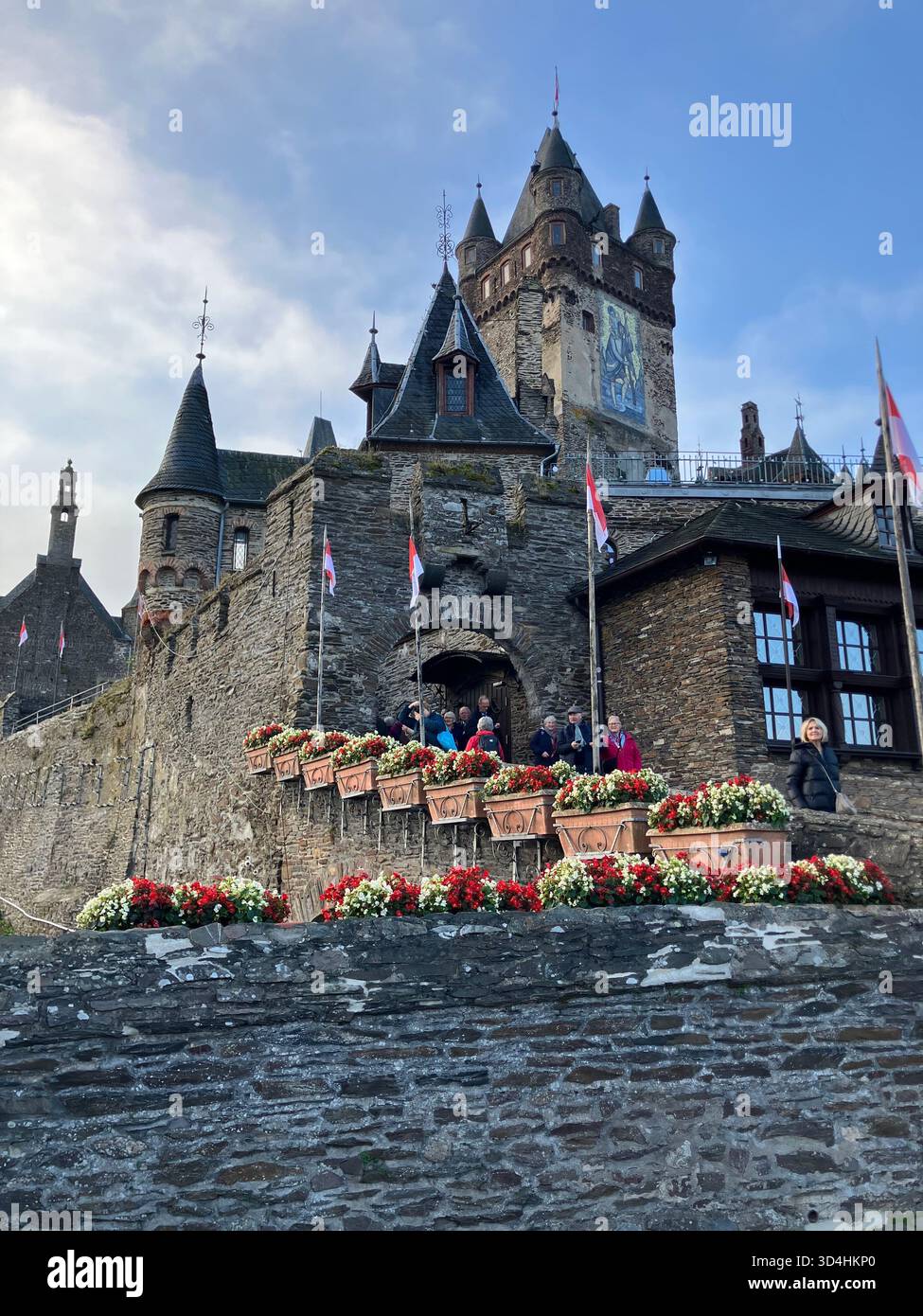 I turisti si radunano vicino alle fioriere lungo l'ingresso in pietra del castello storico di Reichsburg a Cochem, in Germania. Foto Stock