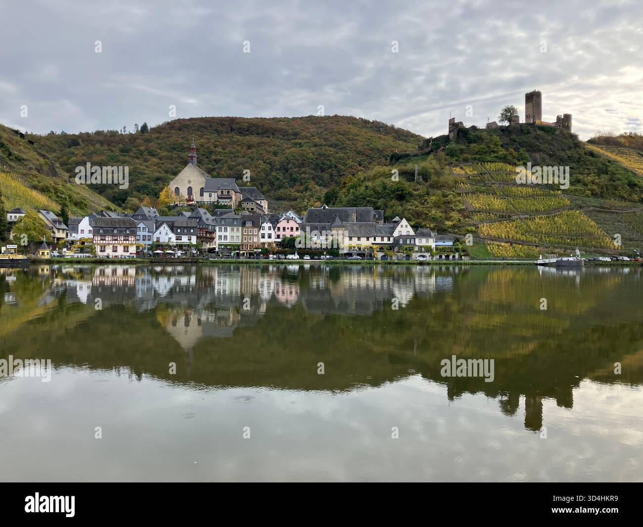 Rovine del castello di Metternich e il villaggio di Beilstein riflessi nel fiume Mosella sotto un cielo nuvoloso a Cochem-Zell, Germania. - Immagine stock catturata con smartphone