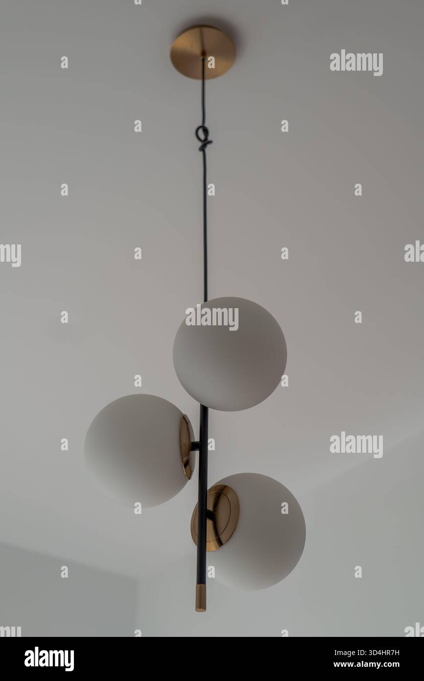 Tre globi opalescenti opalescenti circondano una sottile asta nera con dettagli in ottone in un luminoso appartamento di Danzica, girato verso l'alto con una luce soffusa che dà forma a una tranquilla S Foto Stock