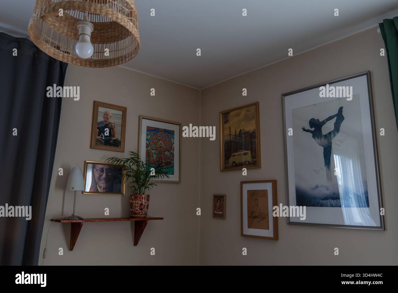 Le calde pareti beige incorniciano opere d'arte eclettiche, una silhouette da ballerina, una stampa gialla in pulmino e abstract. Luce soffusa della finestra, una pianta in vaso e un set di tende in rattan Foto Stock