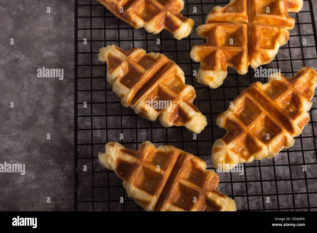I waffle sono disposti su una griglia metallica e rinfrescati in un'accogliente cucina. I caldi waffle dorati hanno una forma unica, che li rende invitanti Foto Stock