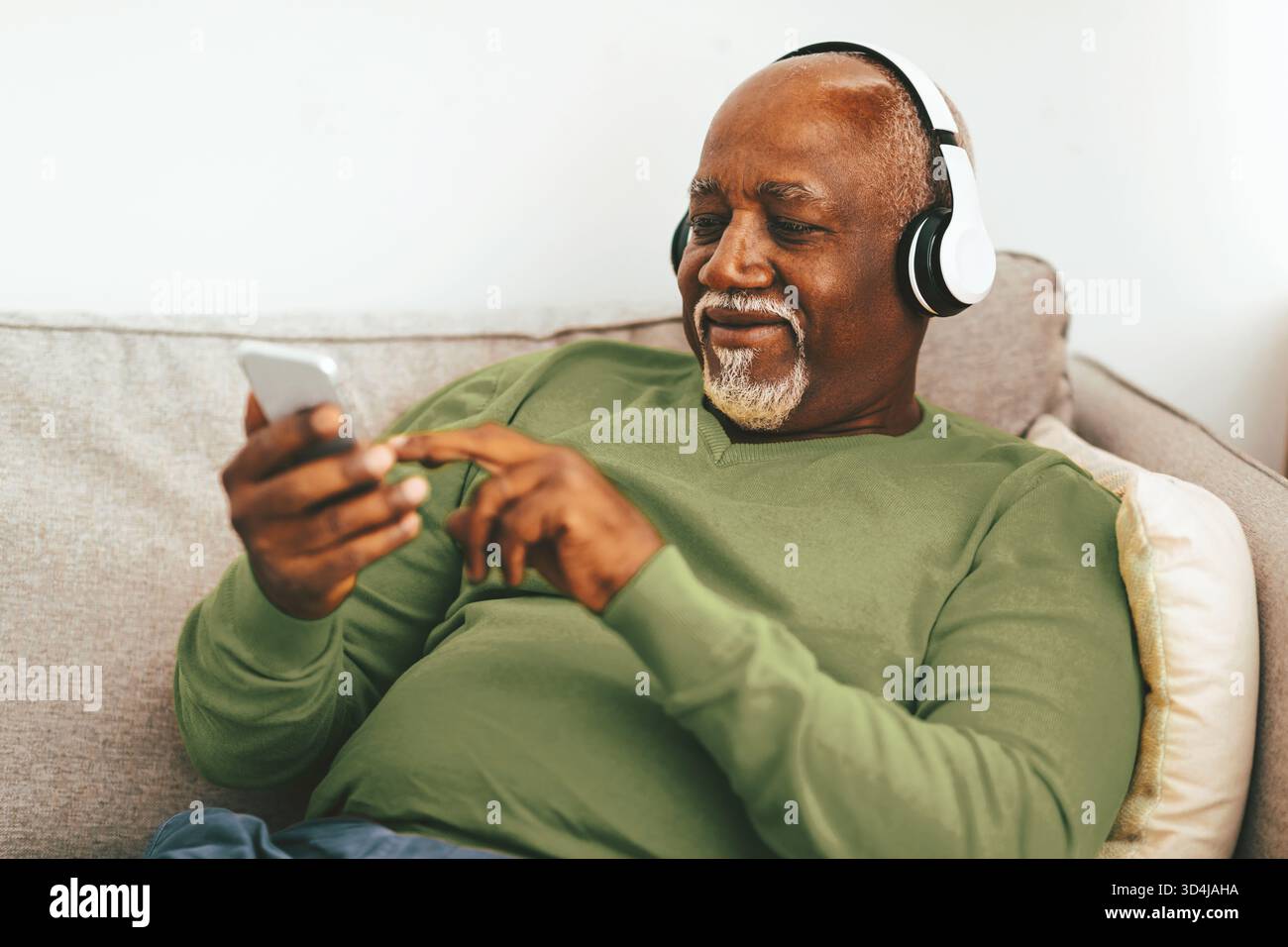 Senior Man ama ascoltare musica mentre si rilassa sul divano a casa durante il pomeriggio Foto Stock