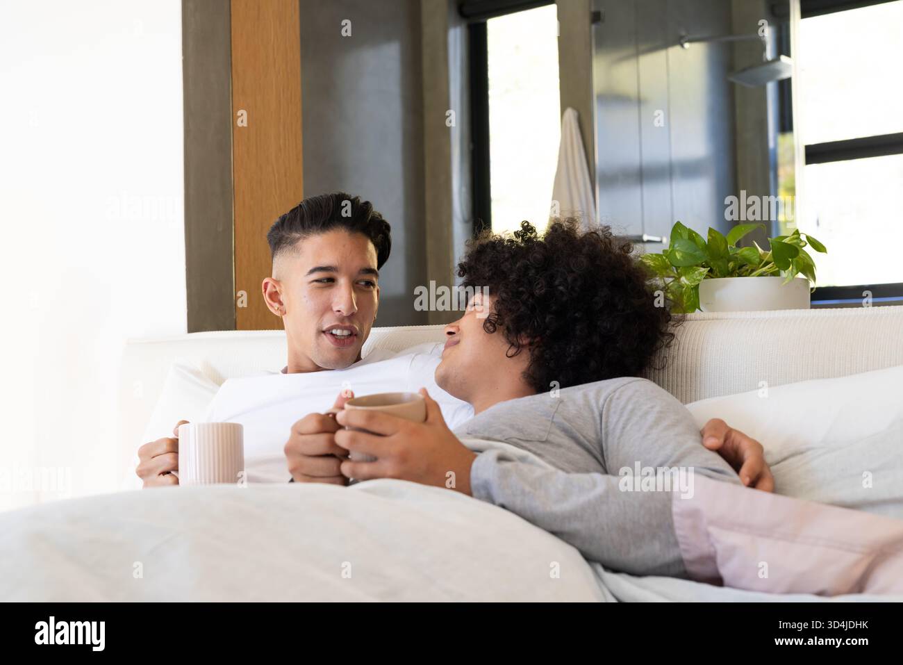 Coccolatevi con diverse coppie di uomini che si trovano insieme sul letto in una camera da letto moderna, con tazze da caffè in ceramica Foto Stock