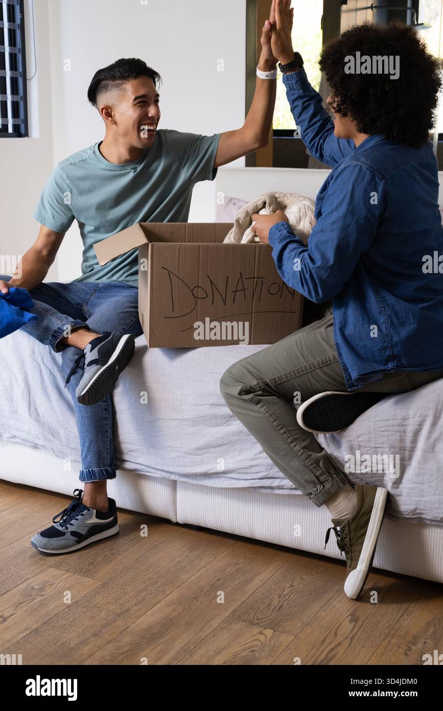 Tanti amici maschi che ordinano donazioni su un divano bianco in una stanza luminosa, con scatola per donazioni Foto Stock