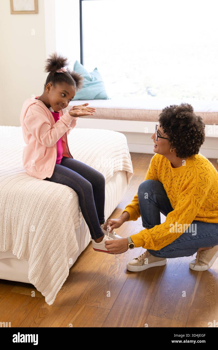 Legando diverse madri e figlie in ginocchio in camera da letto, con sneaker bianche e coperta in maglia Foto Stock