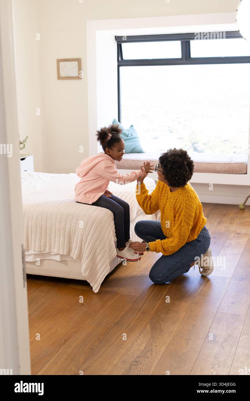 Madre e figlia diverse che si inginocchiano accanto al letto in camera, sneaker bianca regolabile con panca imbottita Foto Stock