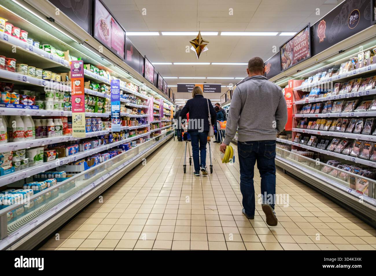 Londra Regno Unito, 10 novembre 2025, Man Walking Down Supermarket Aisle Carry Bunch Bananas Foto Stock