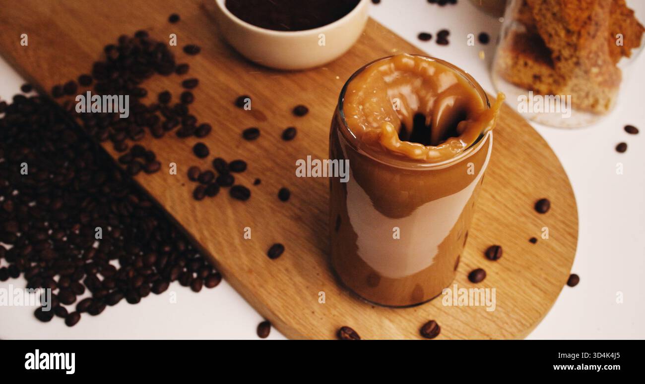 Gusta un bicchiere di caffè e chicchi nella cucina di casa per una bevanda a base di caffeina, colazione e caffè mattutino. Cappuccino, bevanda a base di latte ghiacciato e. Foto Stock