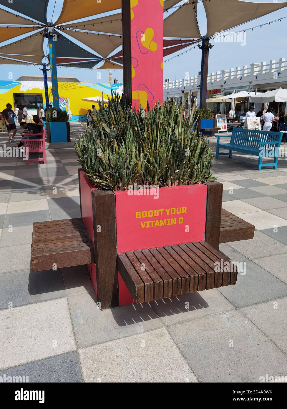 Un luogo di relax soleggiato a Kite Beach Dubai con panchine e simpatico cartello "Boost your Vitamin C", che invita i visitatori a godersi il sole e il tempo libero in riva al mare. Foto Stock