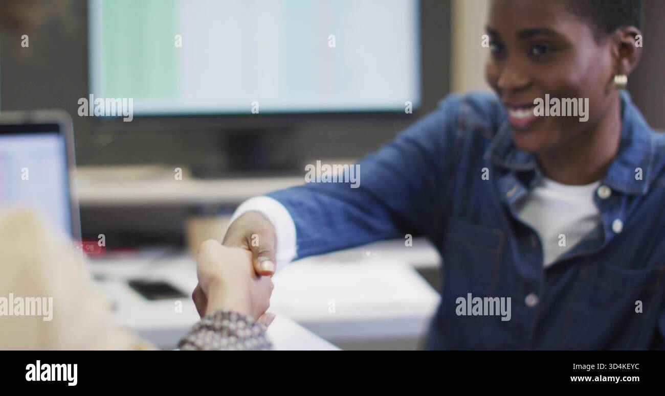 Scuotendo due donne che si scambiano la stretta di mano alla scrivania dell'ufficio, mostrando bracciale con perline, camicia in denim, laptop Foto Stock