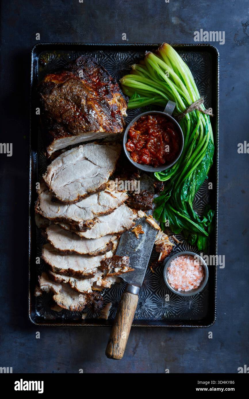 Fotografia gastronomica di alta qualità di arrosto di maiale della Virginia a fette con crosta croccante, salsa di pomodoro, verdure a foglia verde e sale, servito su un vassoio rustico: Ideale Foto Stock