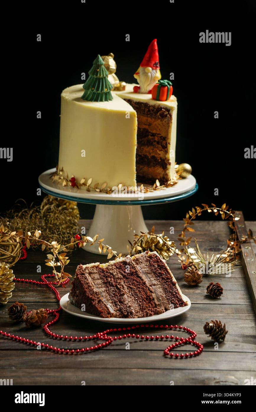 Una moderna torta di Natale su un tavolo da cucina in legno con decorazioni natalizie che la circondano. Foto Stock