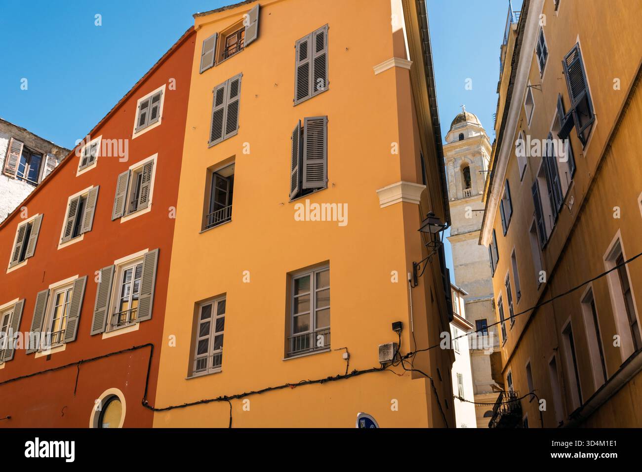 Una delle torri della chiesa di San Giovanni Battista vista attraverso una stretta strada con edifici colorati nella città vecchia, Bastia, Corsica, Francia Foto Stock