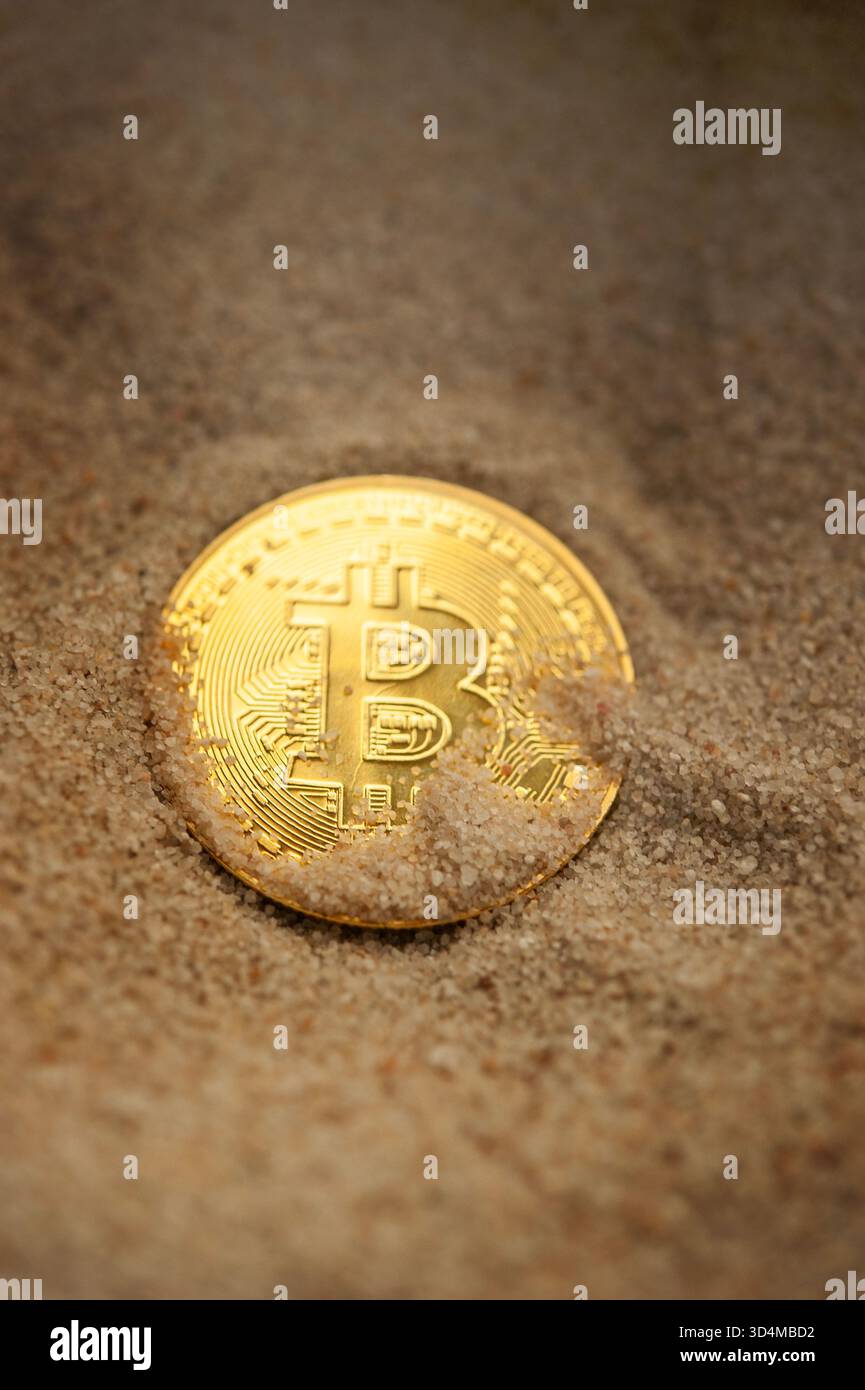 Moneta Bitcoin parzialmente sepolta nella sabbia che simboleggia la ricchezza nascosta, gli investimenti e la volatilità delle criptovalute Foto Stock