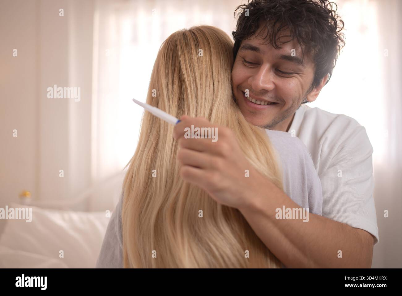 Coppia felice seduta sul letto e sorridente di eccitazione guardando un test di gravidanza positivo || modello rilasciato Foto Stock