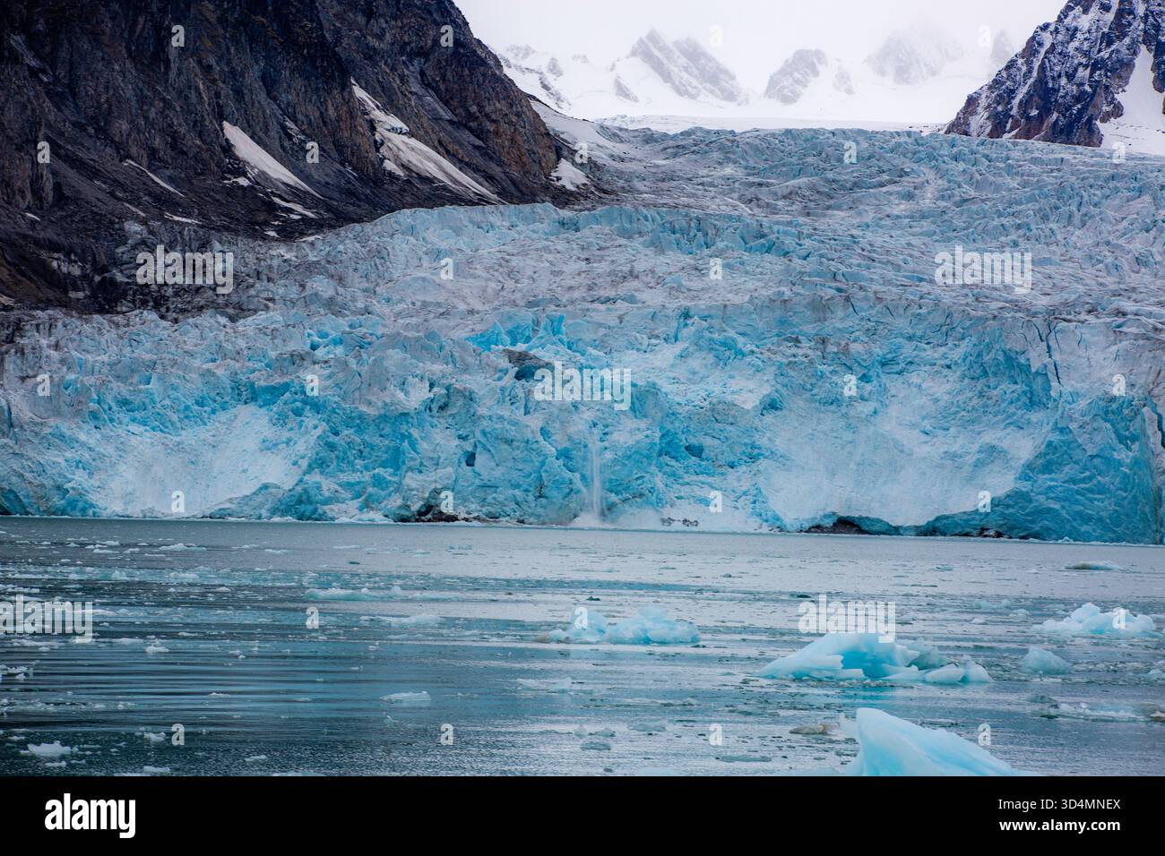 Crociera alle Svalbard - grande parete di ghiaccio blu sullo sfondo di un corpo d'acqua. Il ghiaccio si sta sciogliendo e l'acqua sta diventando più blu Foto Stock