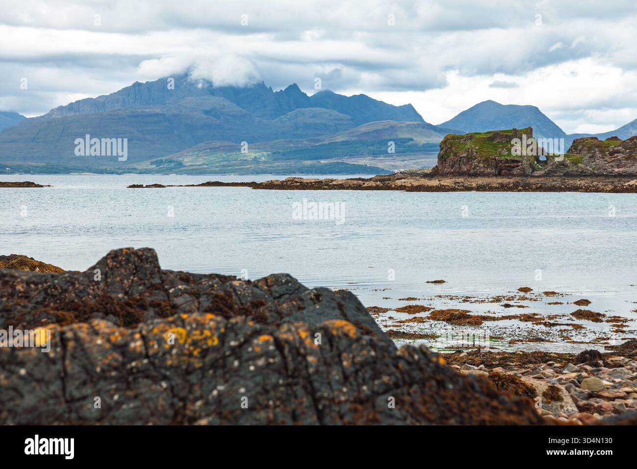 Costa rocciosa con alghe marine e piscine di marea che si affacciano sulle rovine del castello di Dunscaith e sulle montagne Cuillin sull'isola di Skye, Scozia, riflettono il loro splendore Foto Stock