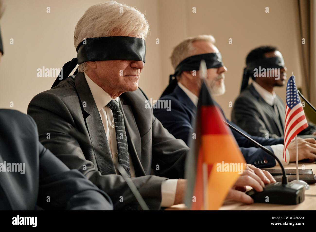 Uomini caucasici anziani e uomo nero seduti bendati al tavolo da conferenza Foto Stock