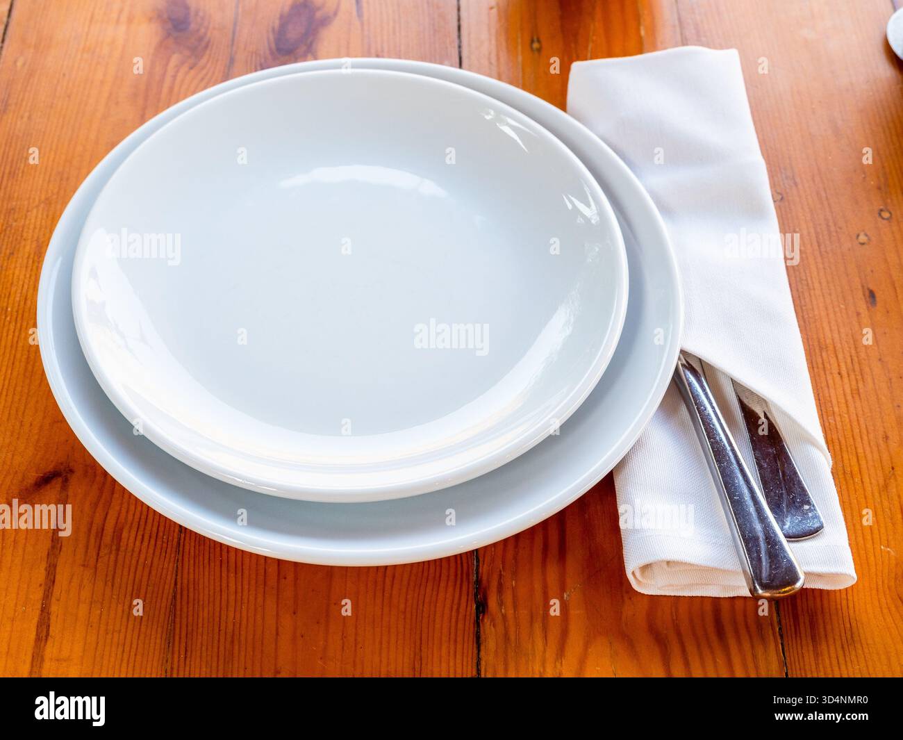 svuotare il piatto bianco nel recipiente, nel coltello e nella forchetta nel tovagliolo servito su un tavolo di legno Foto Stock