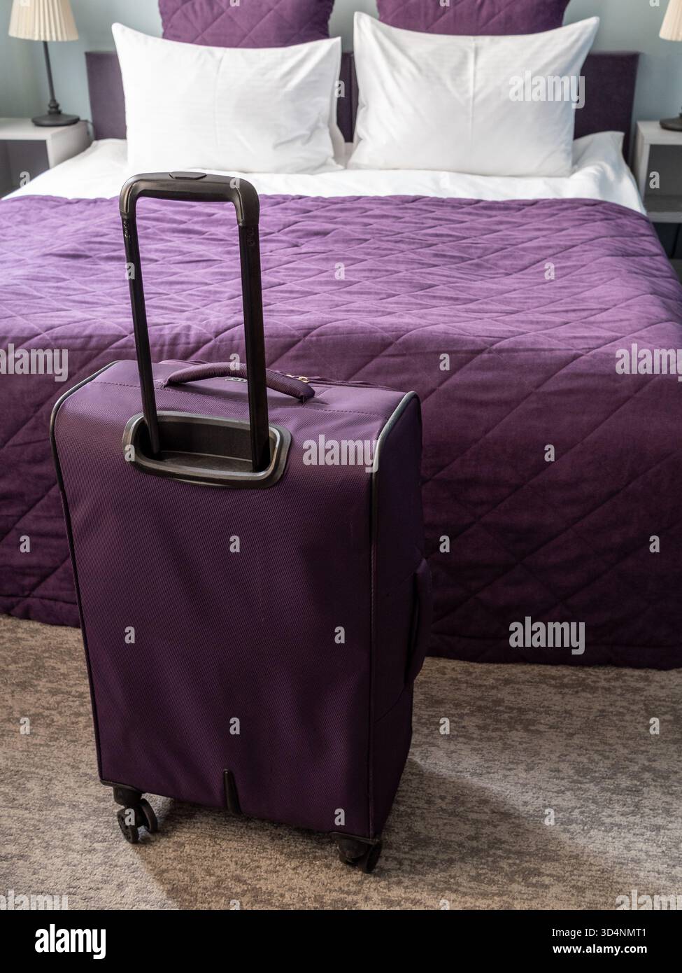valigia da viaggio viola e letto matrimoniale con biancheria bianca e viola in un piccolo soggiorno Foto Stock