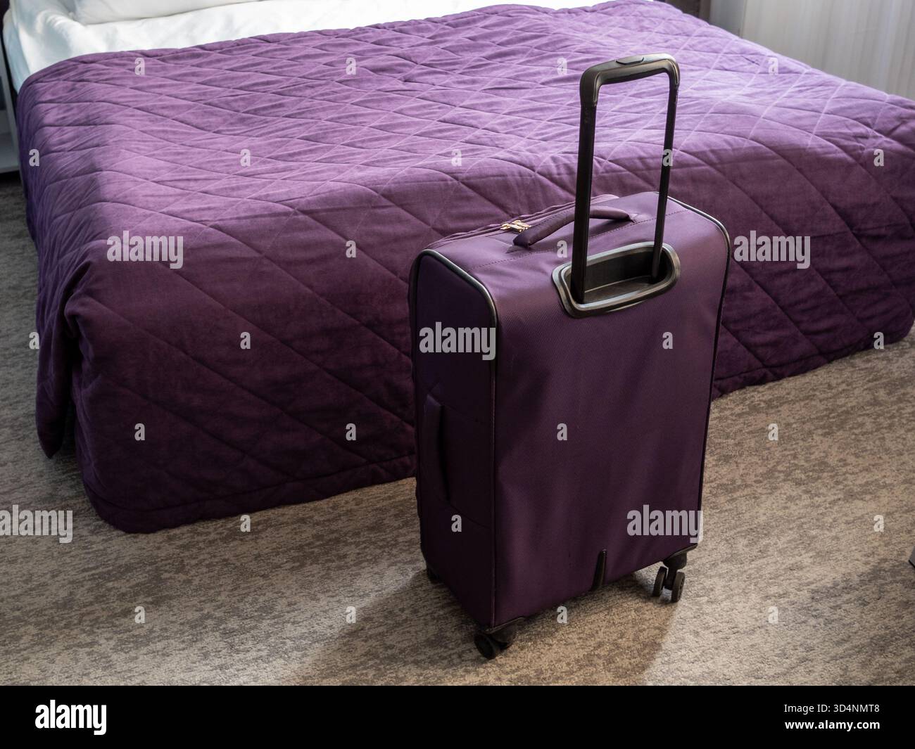 valigia da viaggio viola e copriletto viola su un letto matrimoniale nel piccolo soggiorno Foto Stock