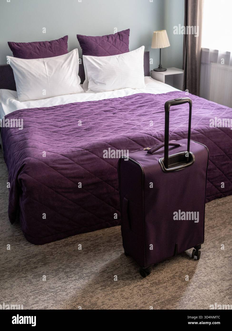 valigia da viaggio viola e letto matrimoniale con biancheria bianca e copriletto viola, con cuscini bianchi e viola nel piccolo soggiorno Foto Stock