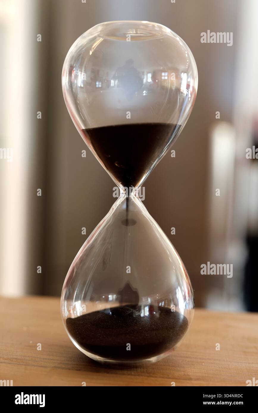 Clessidra con il tempo che sta per scadere su un tavolo. Concetto di passaggio del tempo. Foto Stock