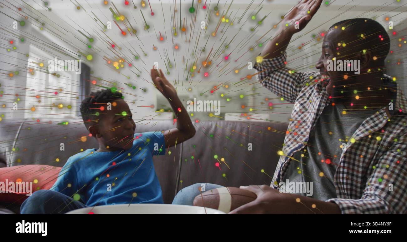 Papà e figlio dai toni alti sul divano grigio di casa, maglietta blu a quadri, calcio e ciotola, coriandoli Foto Stock