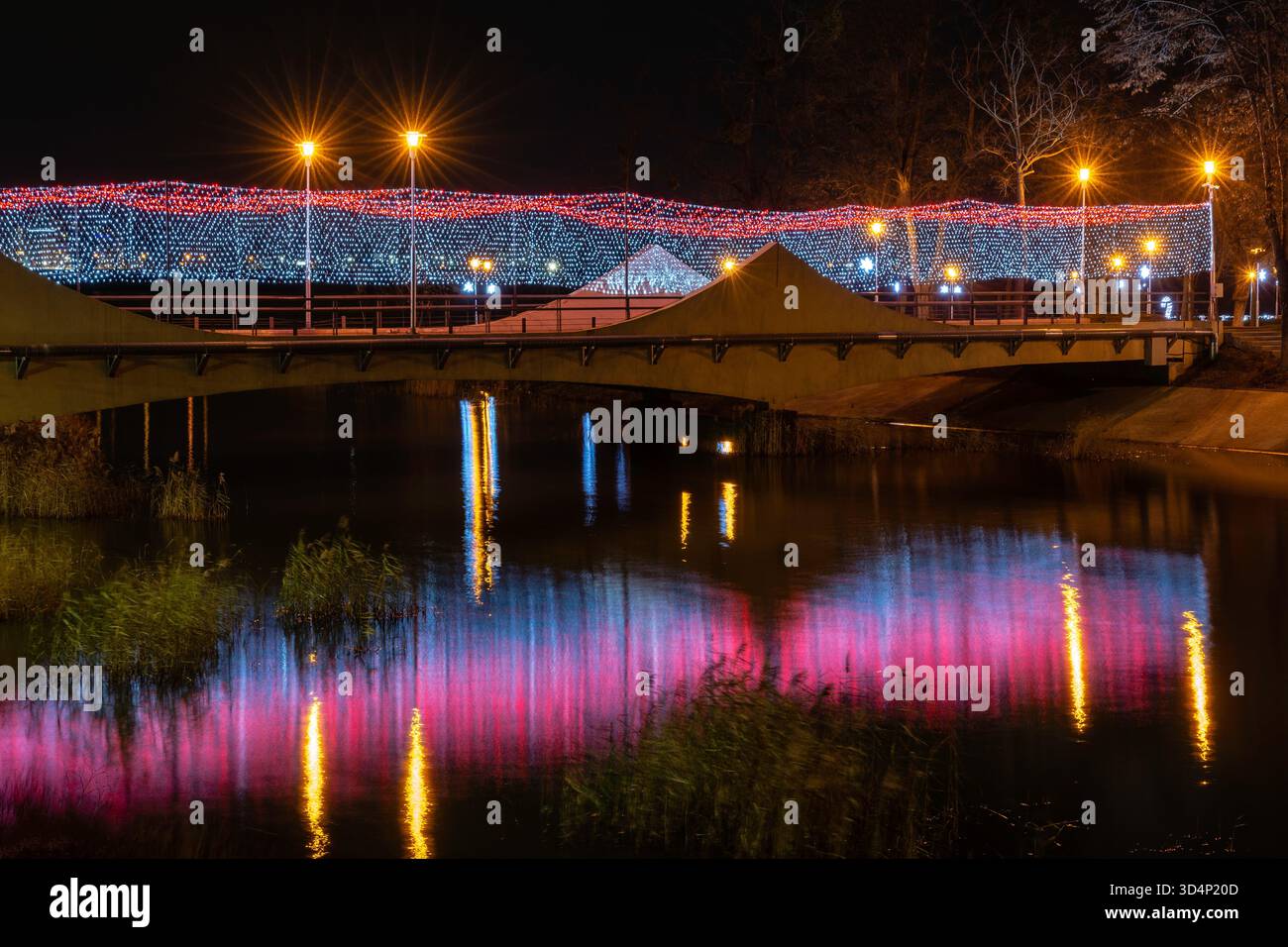 Ponte sull'acqua di notte con luci festose a griglia e riflessi caldi in un ambiente naturale. Foto Stock