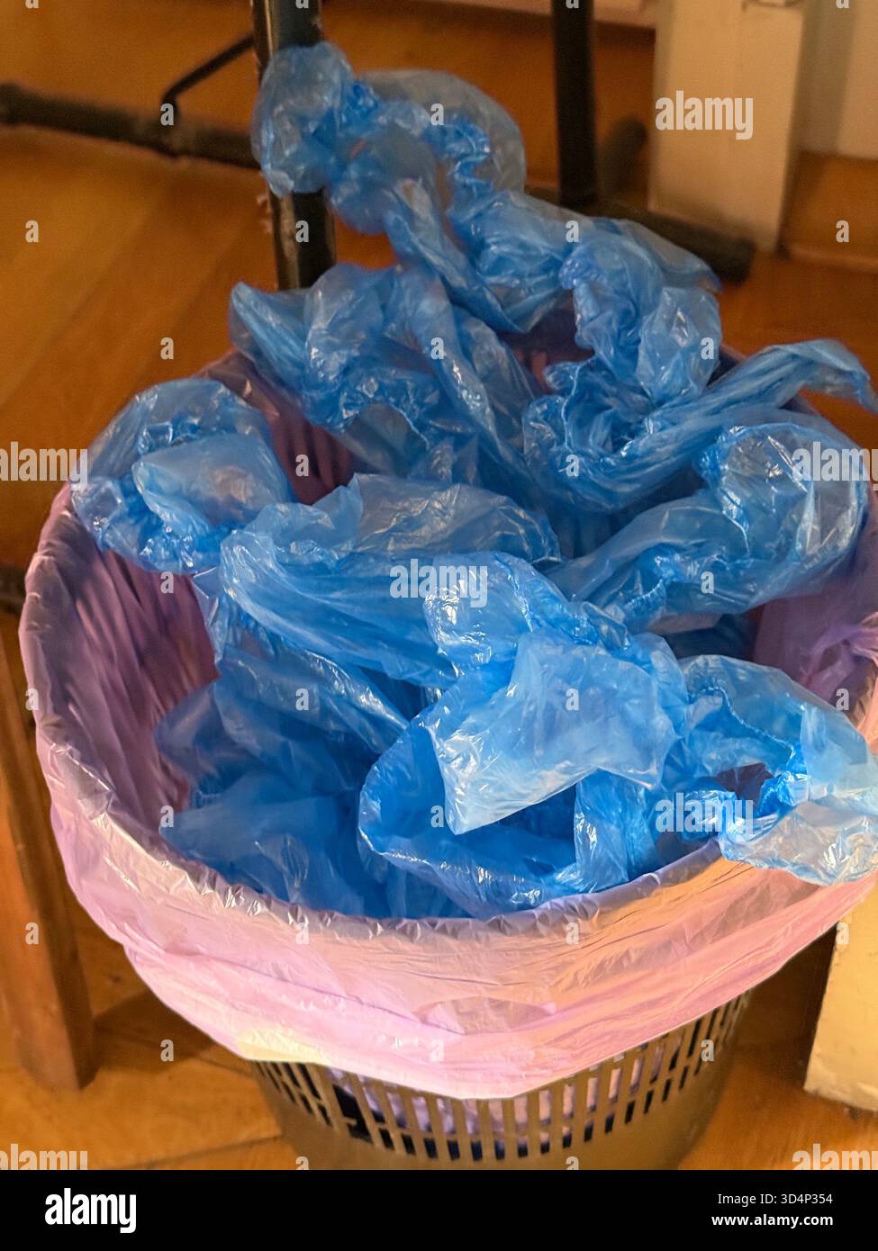 Rifiuti di plastica in un contenitore viola con sacchetti blu al chiuso, evidenziando i problemi ambientali. Foto mobile Foto Stock