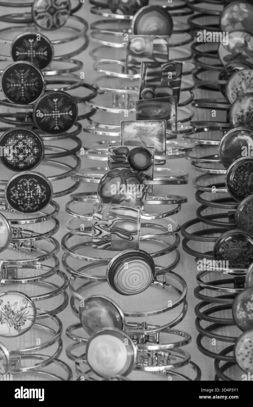 Una fotografia monocromatica che mostra una serie di bracciali in metallo realizzati a mano disposti in modo ordinato per essere esposti. I motivi e le trame artistiche evidenziano t Foto Stock