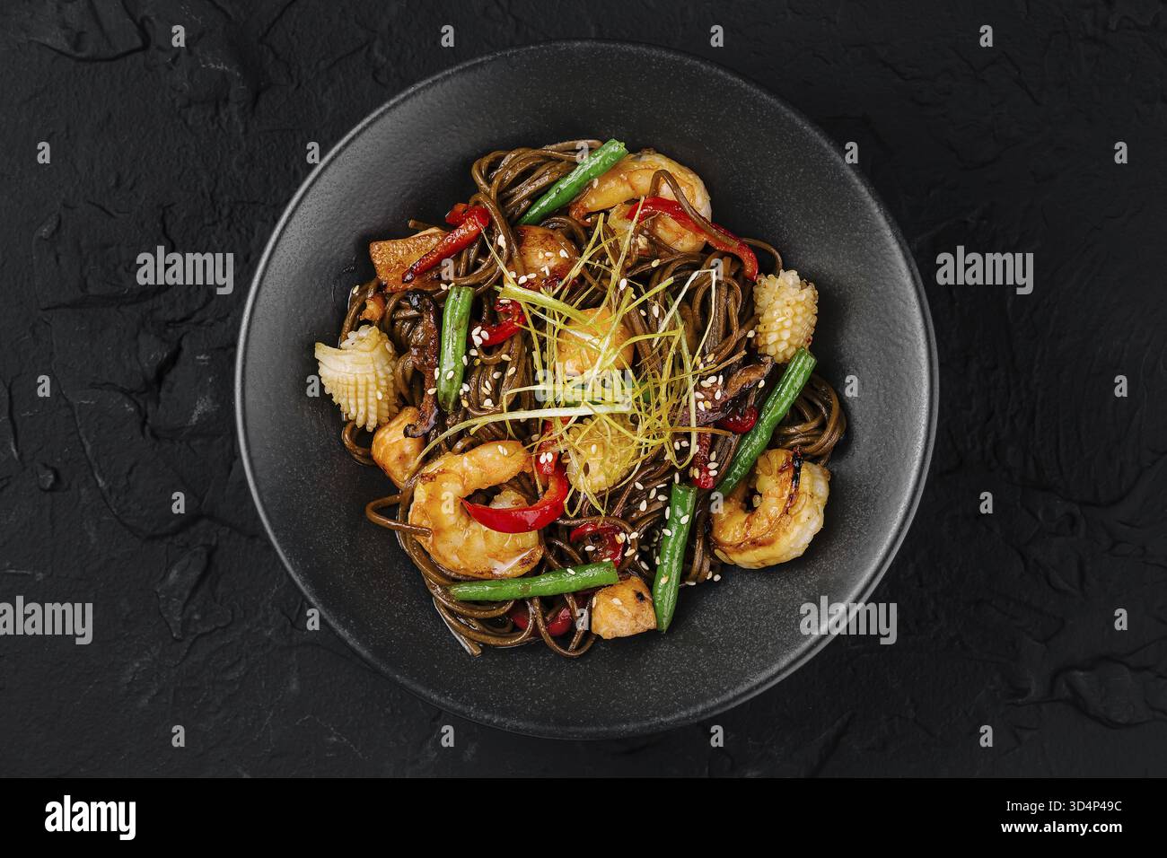 Cibo, cucina asiatica: Spaghetti saltati in padella con gamberi, verdure e guarnire in una ciotola nera su uno sfondo scuro Foto Stock