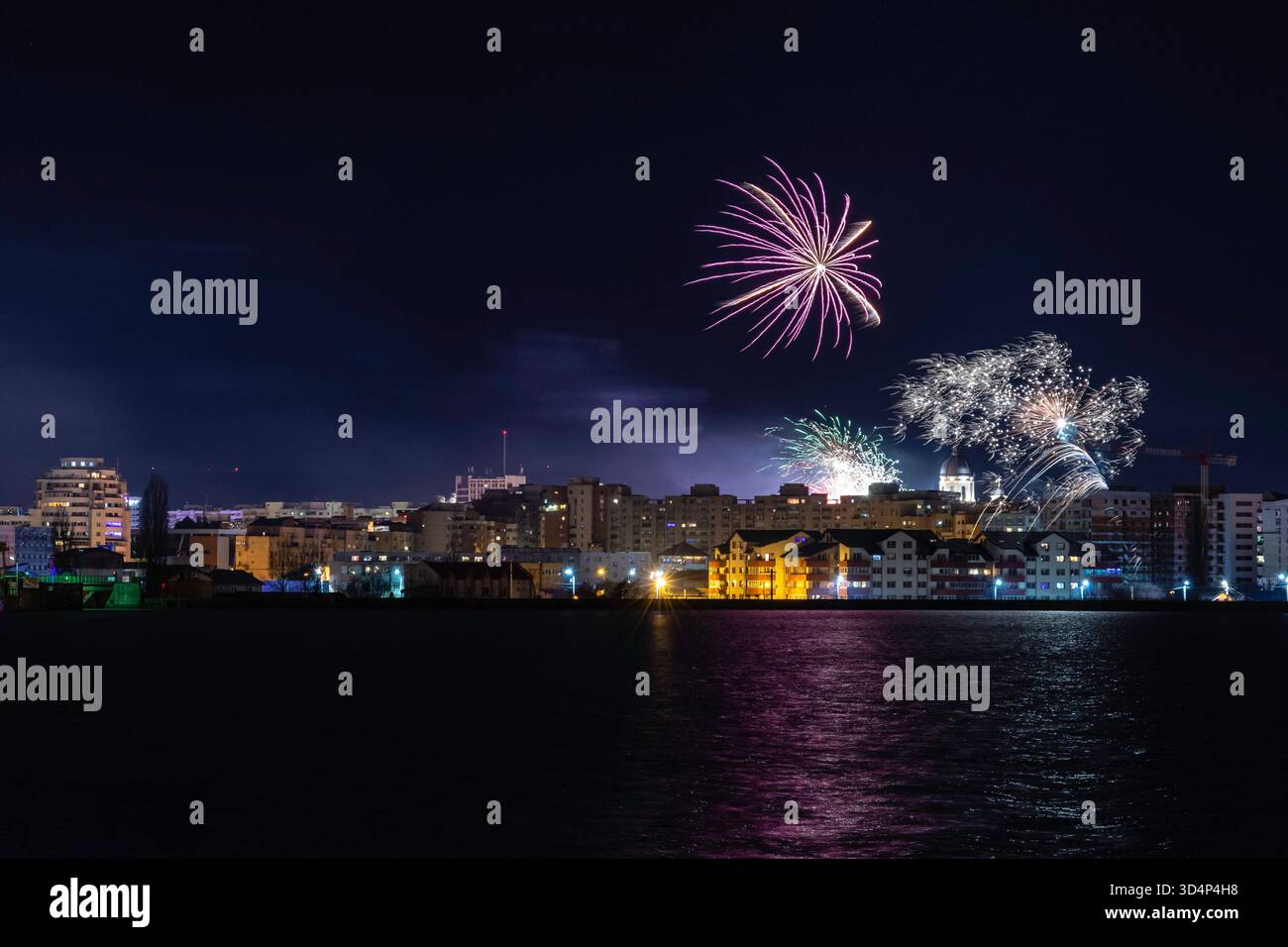 I fuochi d'artificio gialli e viola illuminano il cielo notturno sopra gli edifici della città e la cupola della chiesa. Una scena di festa. Foto Stock