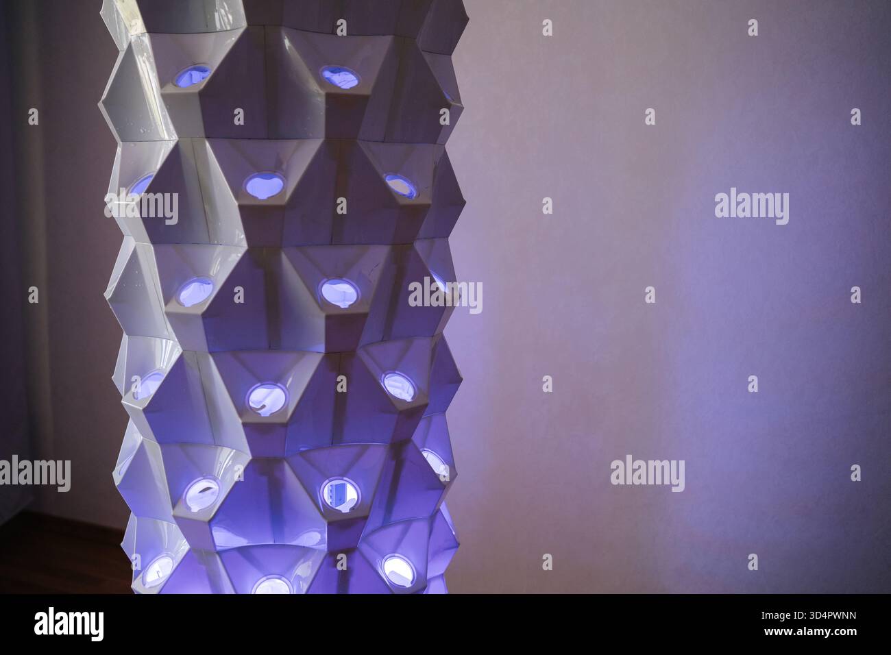 Torre idroponica verticale con luci blu che illuminano la struttura geometrica che mette in risalto l'innovativa tecnologia agricola per interni Foto Stock