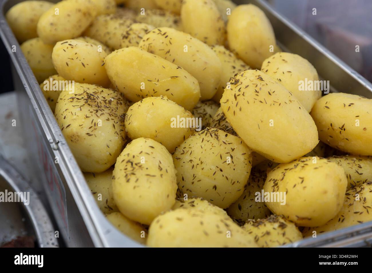 Primo piano di patate bollite condite con il cumino o altre erbe aromatiche in un vassoio di metallo Foto Stock