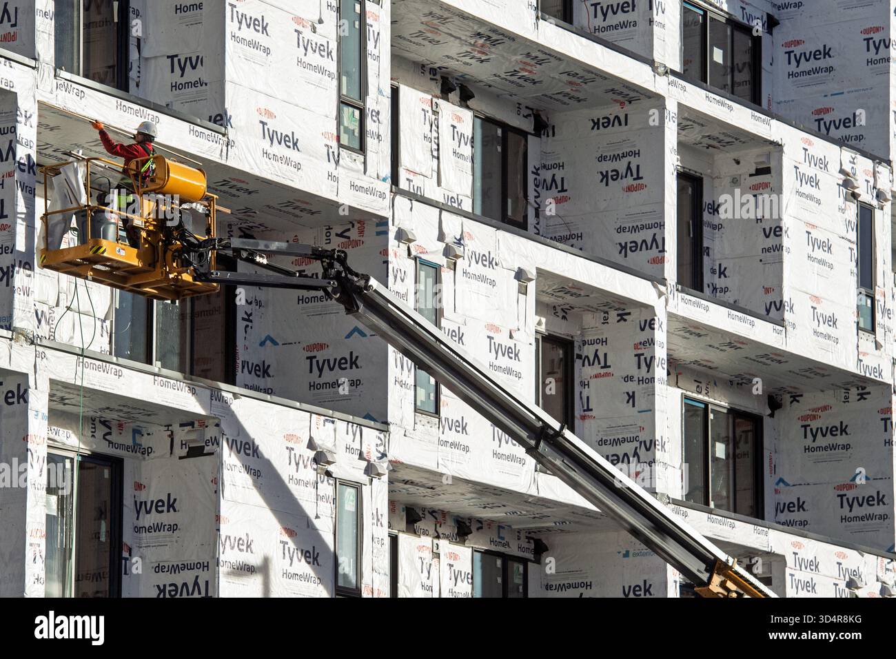 Operaio edile che opera da un ascensore accanto a un edificio avvolto in Tyvek HomeWrap Foto Stock