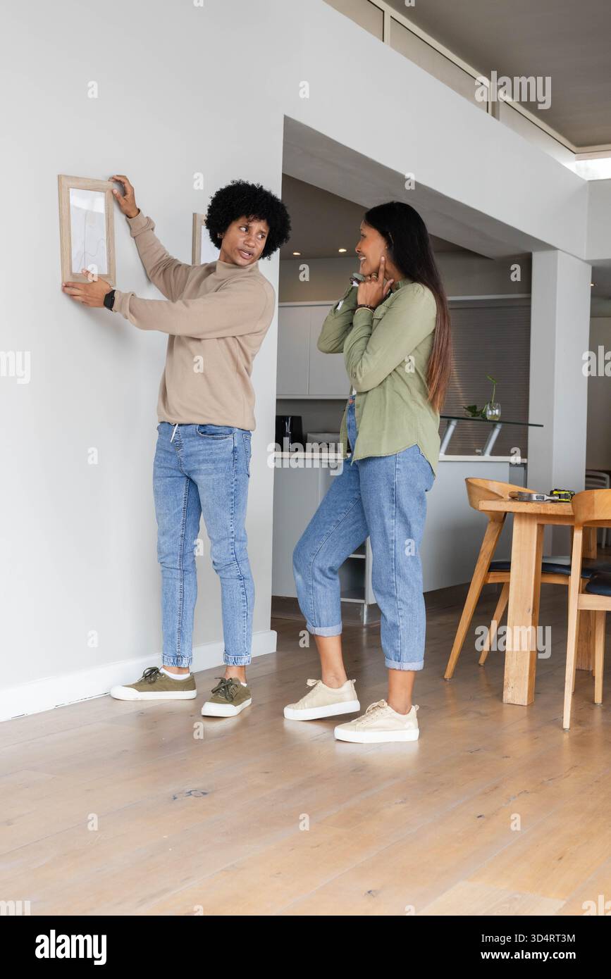 Appendere diverse coppie posizionare la cornice sulla parete in una casa a pianta aperta, con un metro a nastro sul tavolo Foto Stock