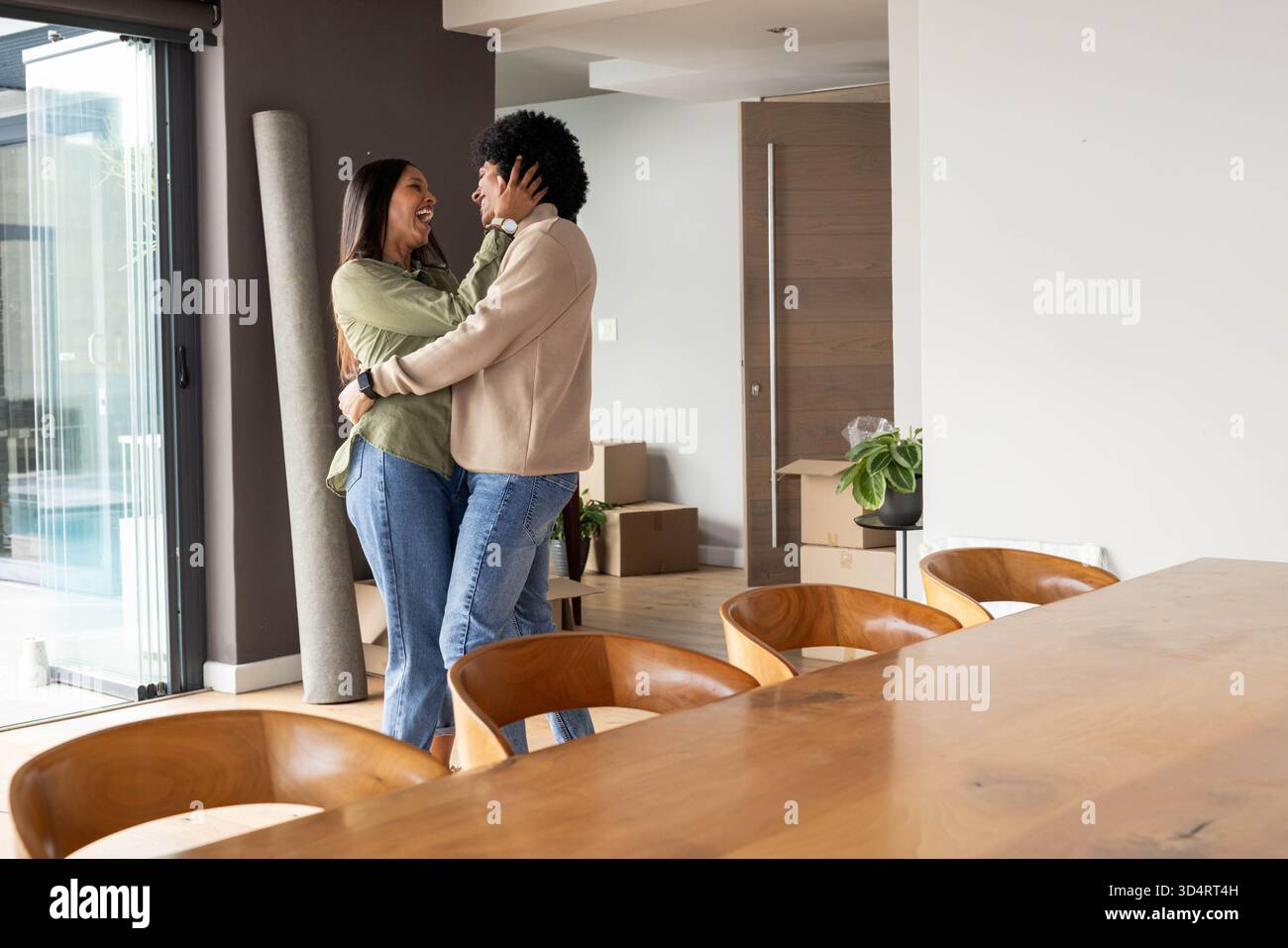 Abbracciare coppie diverse che si sistemano in una casa a pianta aperta, con scatole mobili e tavolo, spazio di copia Foto Stock