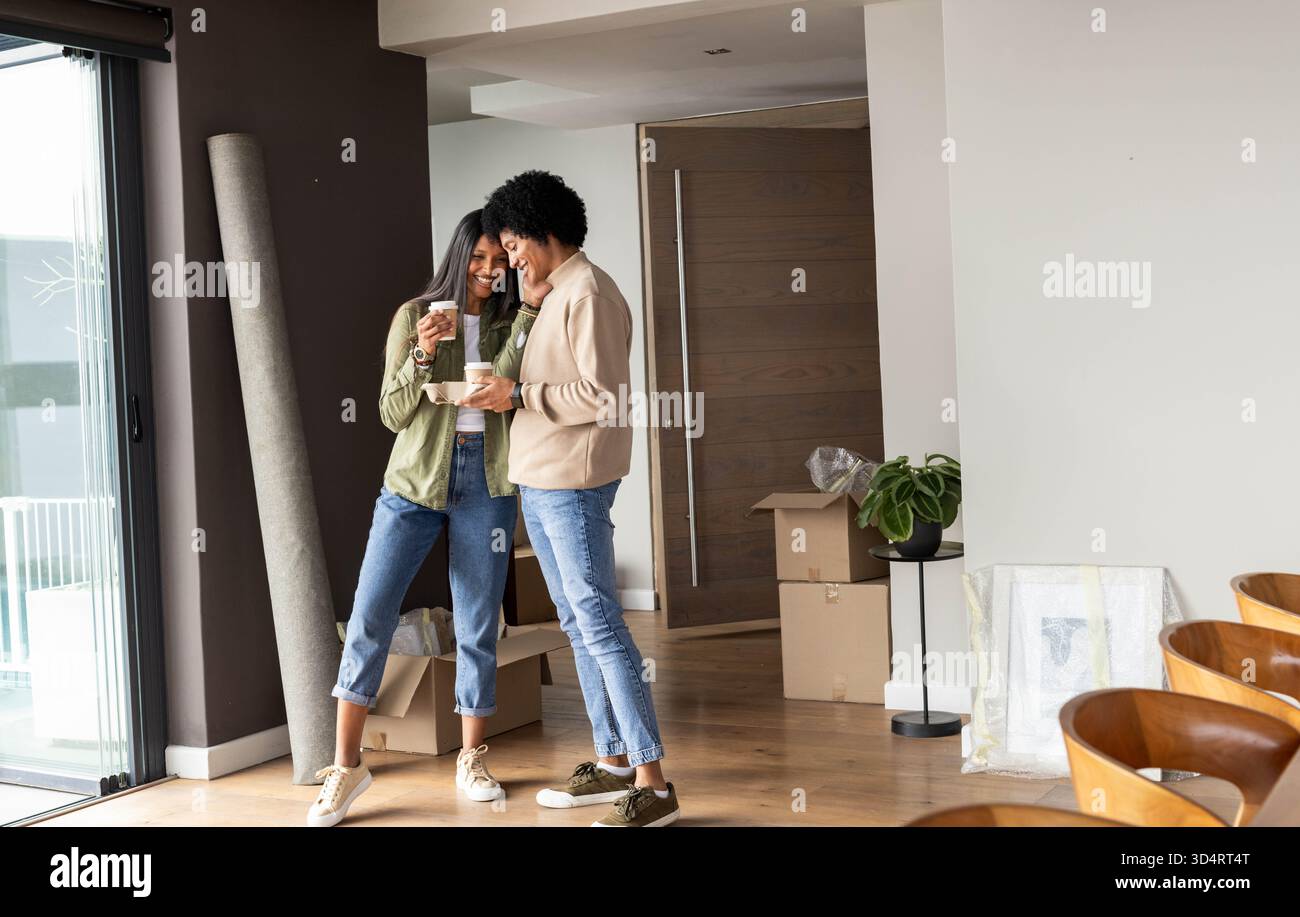 Una coppia di persone diverse che tengono tazze da caffè all'interno di una moderna zona soggiorno dell'appartamento, con scatole mobili Foto Stock