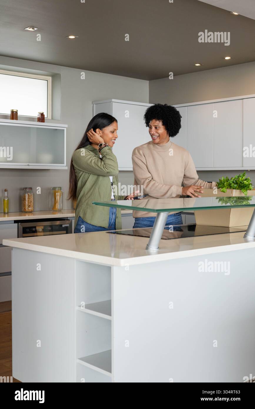 Coppia di persone sorridenti in piedi in una cucina moderna, con ripiano in vetro rialzato e pianta in vaso Foto Stock